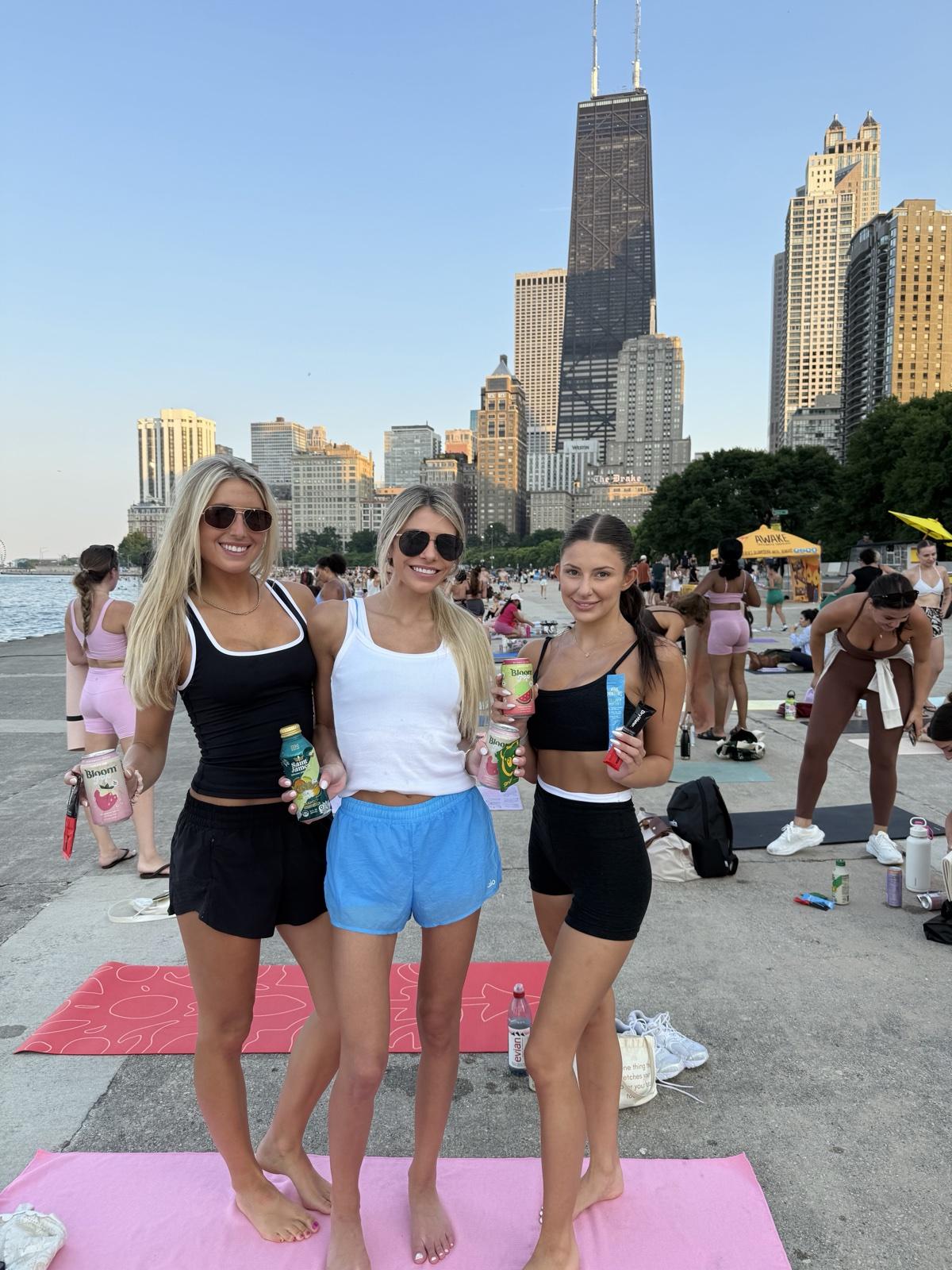 Members holding Bloom, Saint James, and DryWater products together at a lakefront event with the Chicago skyline behind them
